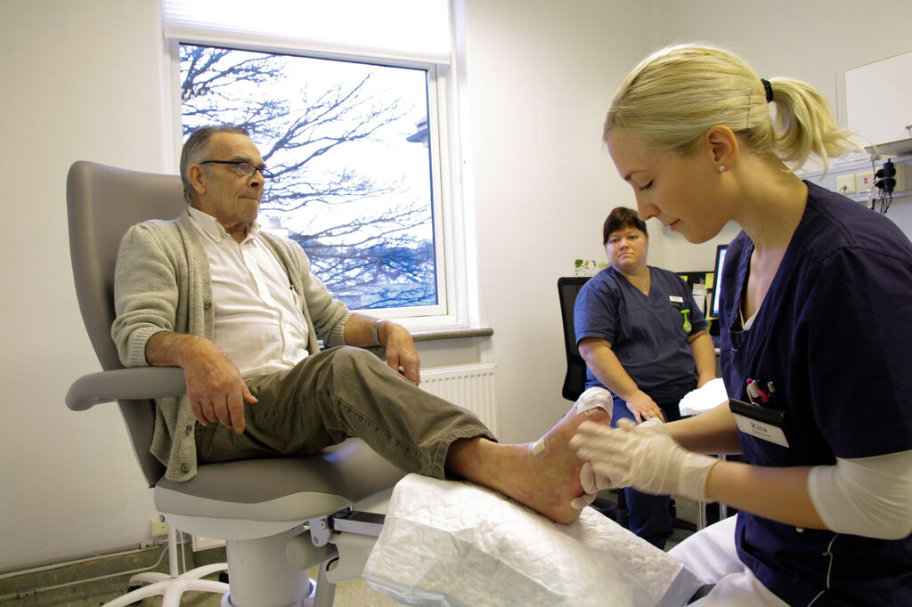 Bildet viser en sykepleier som utfører sårstell på en pasient ved Stavanger helsehus. En annen sykepleier observerer.