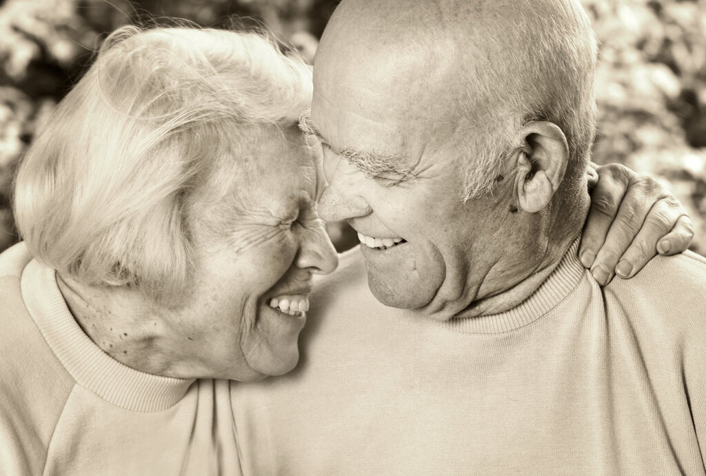 Bildet viser en eldre kvinne som holder rundt en eldre mann. De smiler.