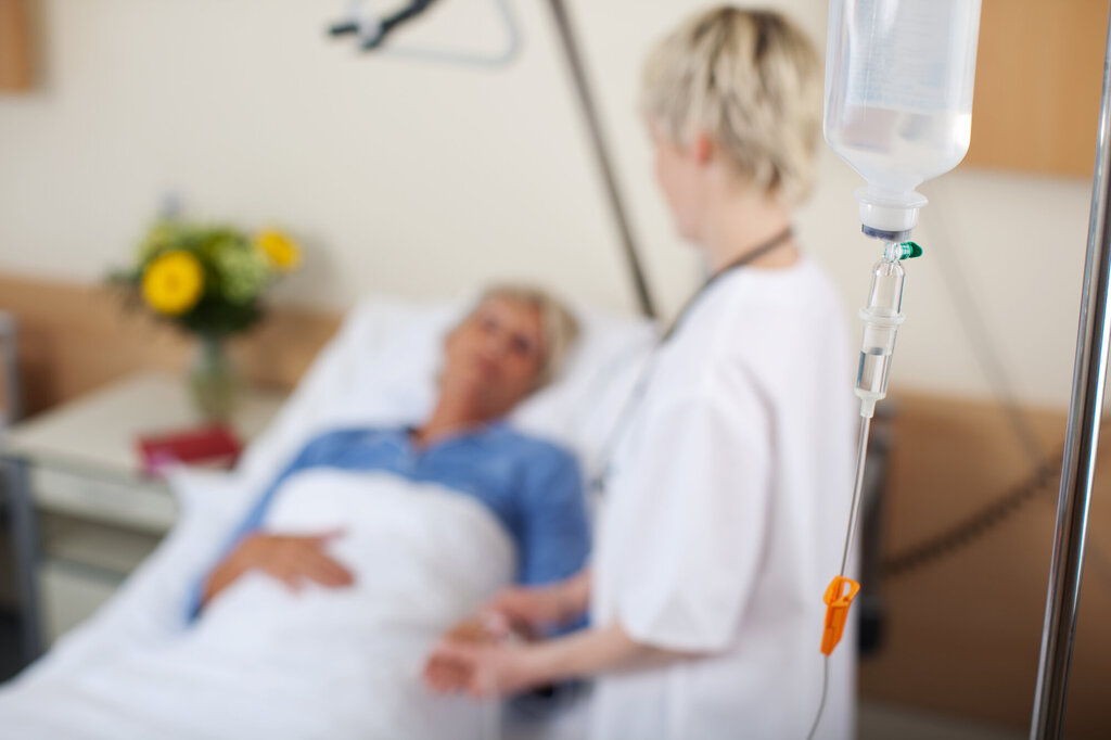 Bildet viser en sykepleier som står ved siden av en sengeliggende pasient
