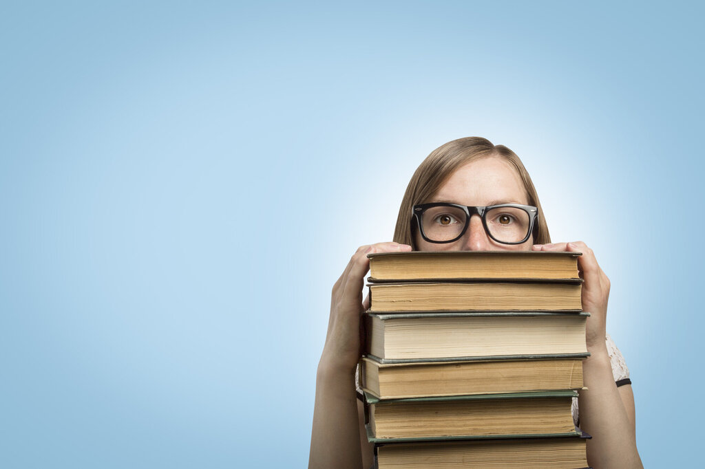 Bildet viser en student som titter opp over en stabel av bøker