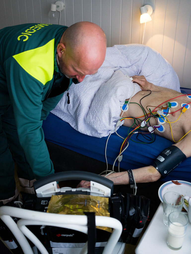bildet viser Lundli som tar EKG på pasient som ligger hjemme