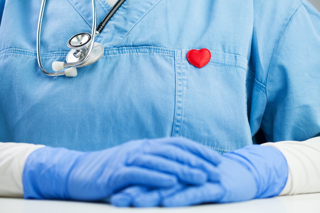 Bildet viser utsnitt av en sykepleier. På brystet har vedkommende et rødt hjerteformet emblem 
