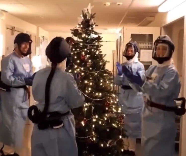 Bildet viser sykepleiere i smittevernutstyr som går rundt juletreet