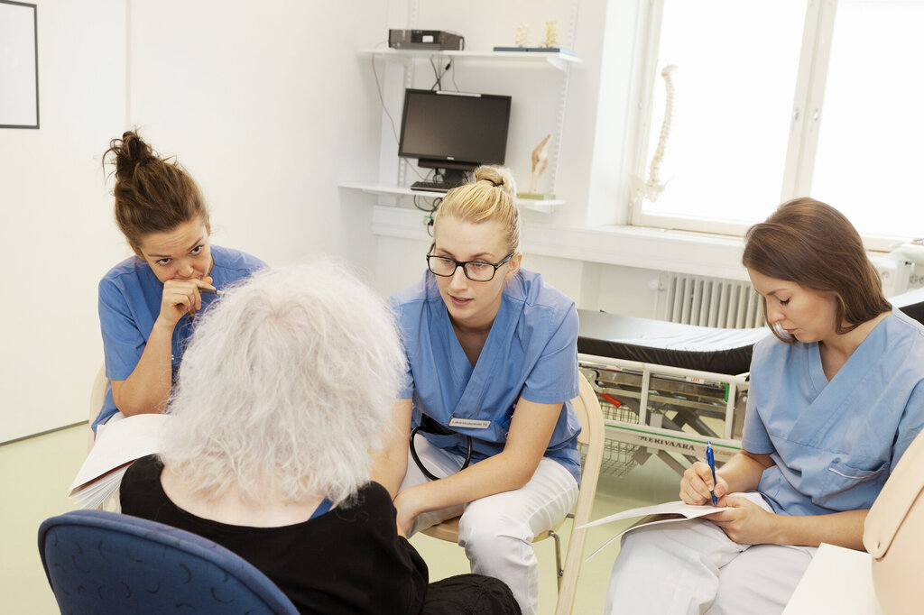 Bildet viser tre sykepleierstudenter som lytter og noterer mens en lærer snakker.