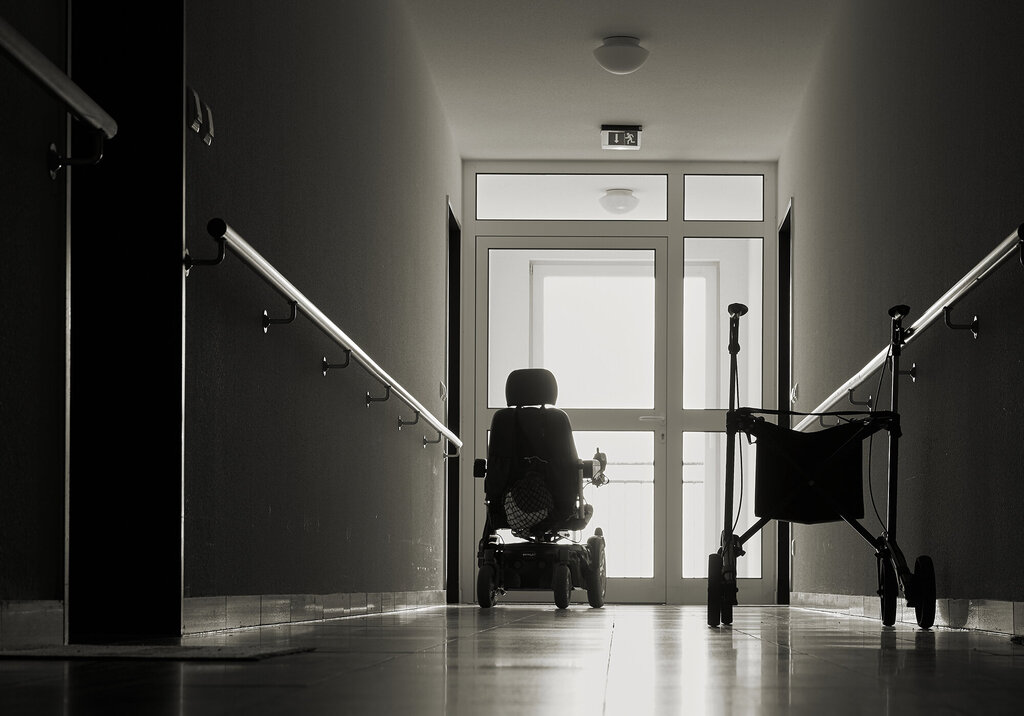 Bildet viser en sykehjemsbeboer i rullestol som sitter ved vinduet i enden av en korridor