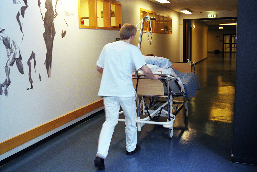 Bildet viser en mannlig sykepleier som triller en pasientseng i sykehus