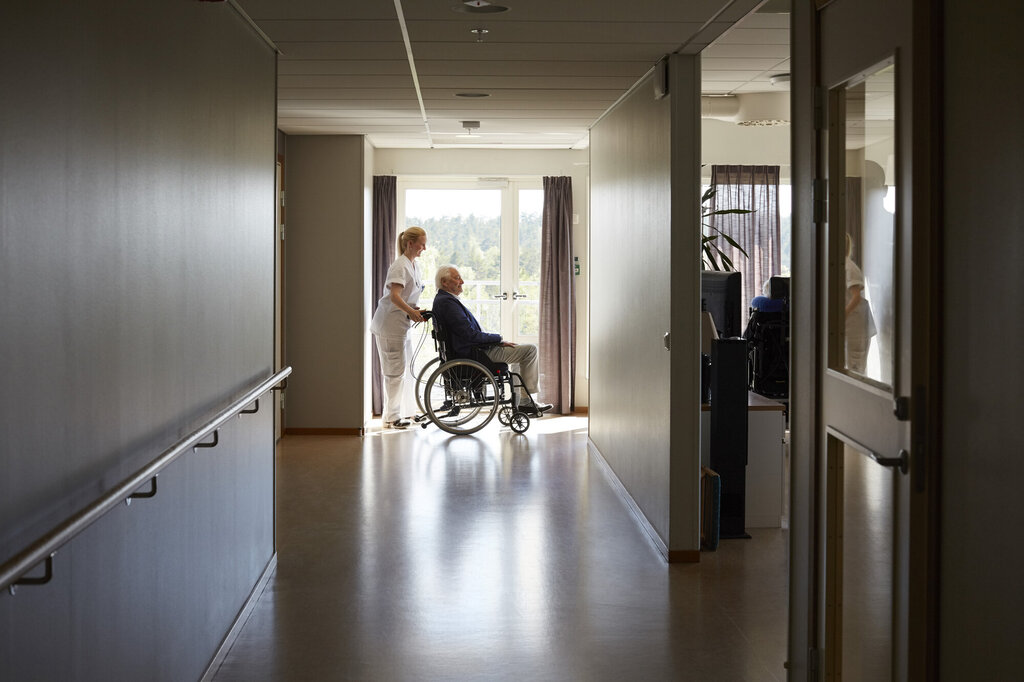 Bildet viser en sykepleier som triller en pasient i rullestol på et bo- og behandlingssenter