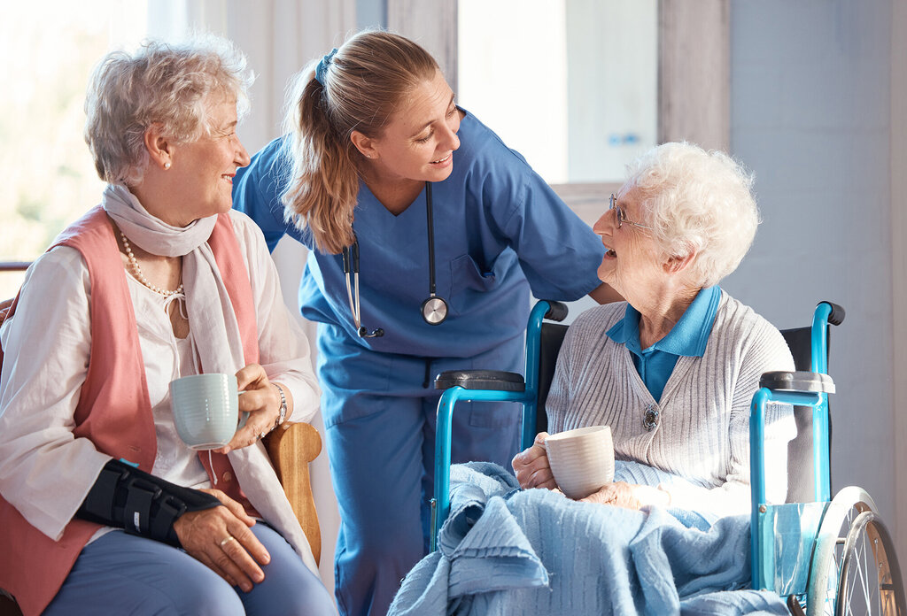 Bildet viser en sykepleier som snakker med to eldre beboere på et sykehjem
