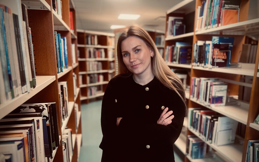 Bildet viser Cathrine Emilie Valgermoe Forren. Hun står i et bibliotek, ser mot kamera og har armene i kors.