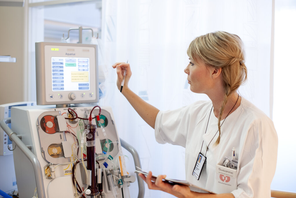 The photo shows an intensive care nurse touching a screen on a machine with tubes and other equipment.
