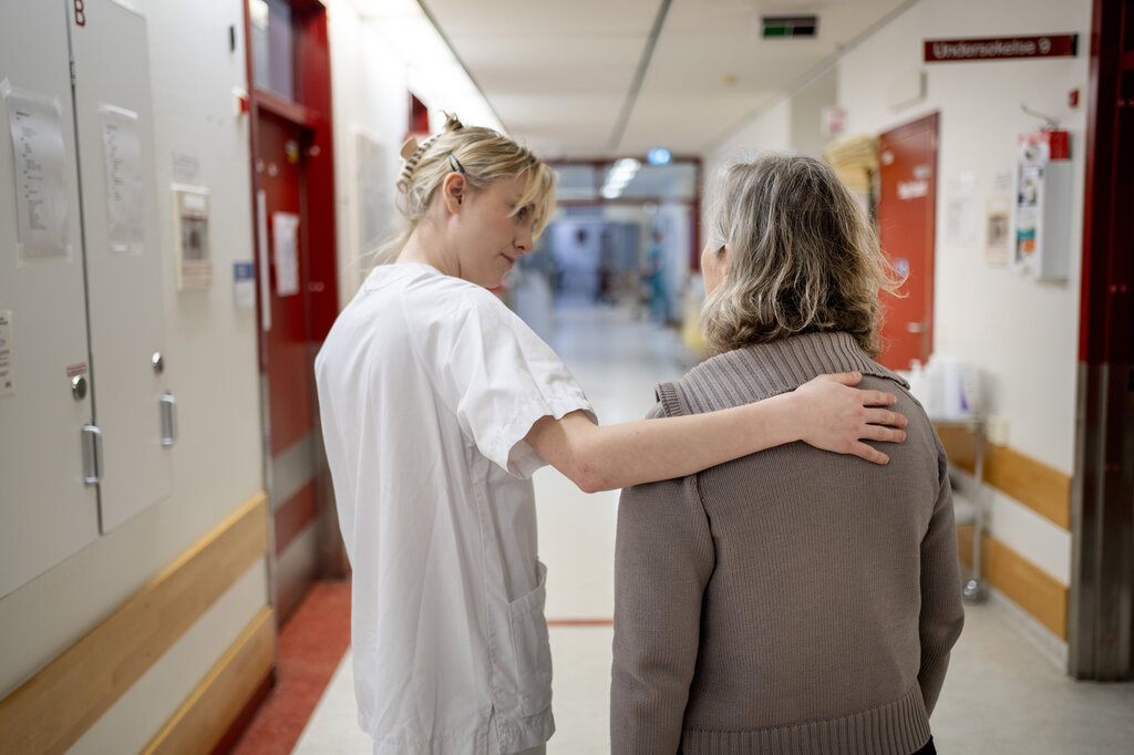 Bildet viser en ung, kvinnelig sykepleier som har hånden på ryggen til en pasient