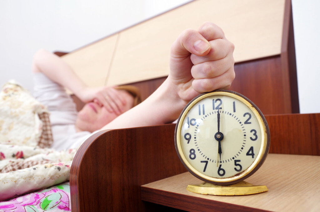 Bildet viser en kvinne som nettopp har våknet av vekkeklokken og slår av alarmen