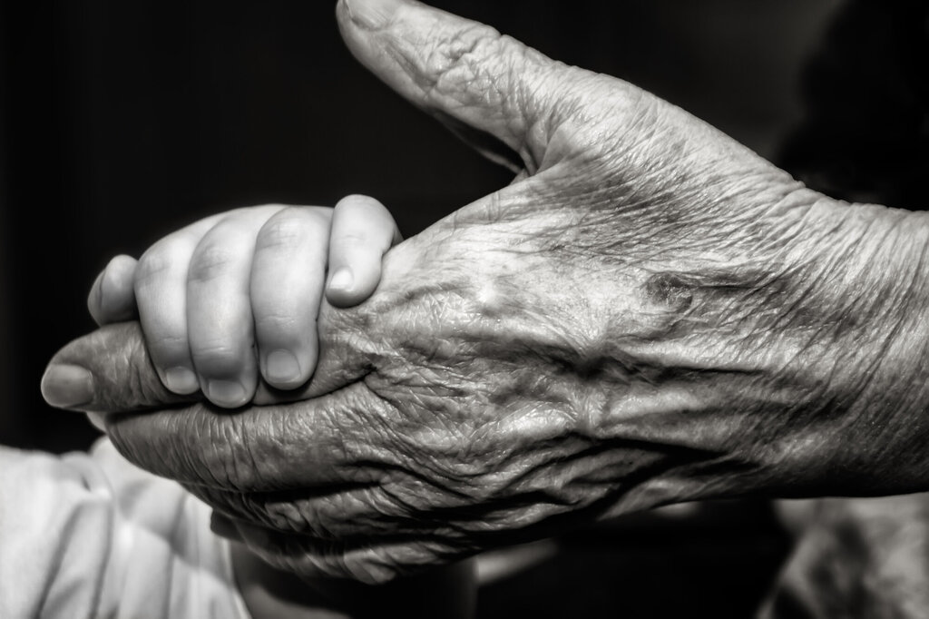 Bildet viser et lite barn som holder et gammelt menneske i hånden.