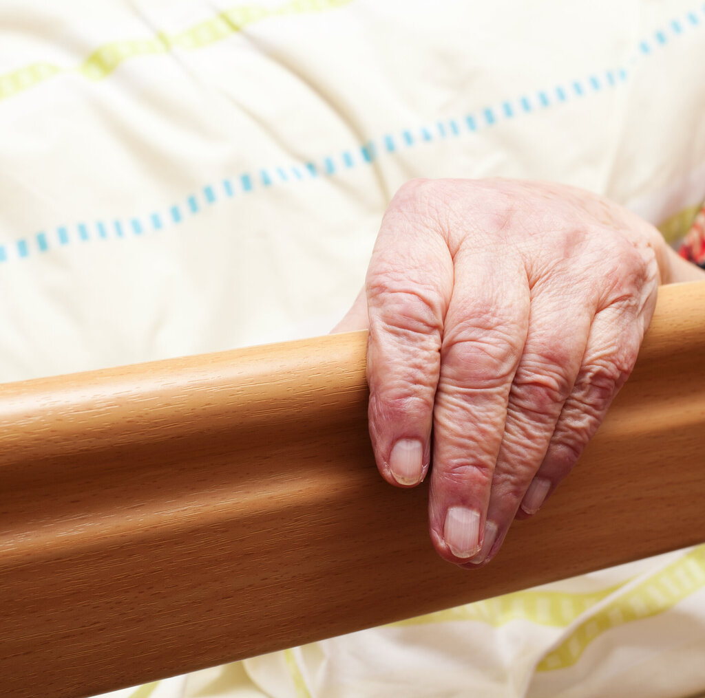 Bildet viser en hånden til en eldre mann som ligger i sengen på et pleiehjem.