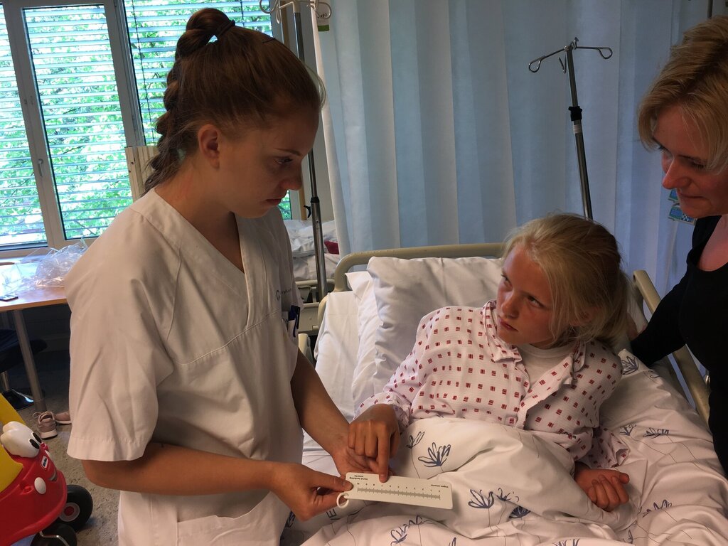 En ungdom på sykehuset forklarer sykepleier hvor vondt hun har det. 