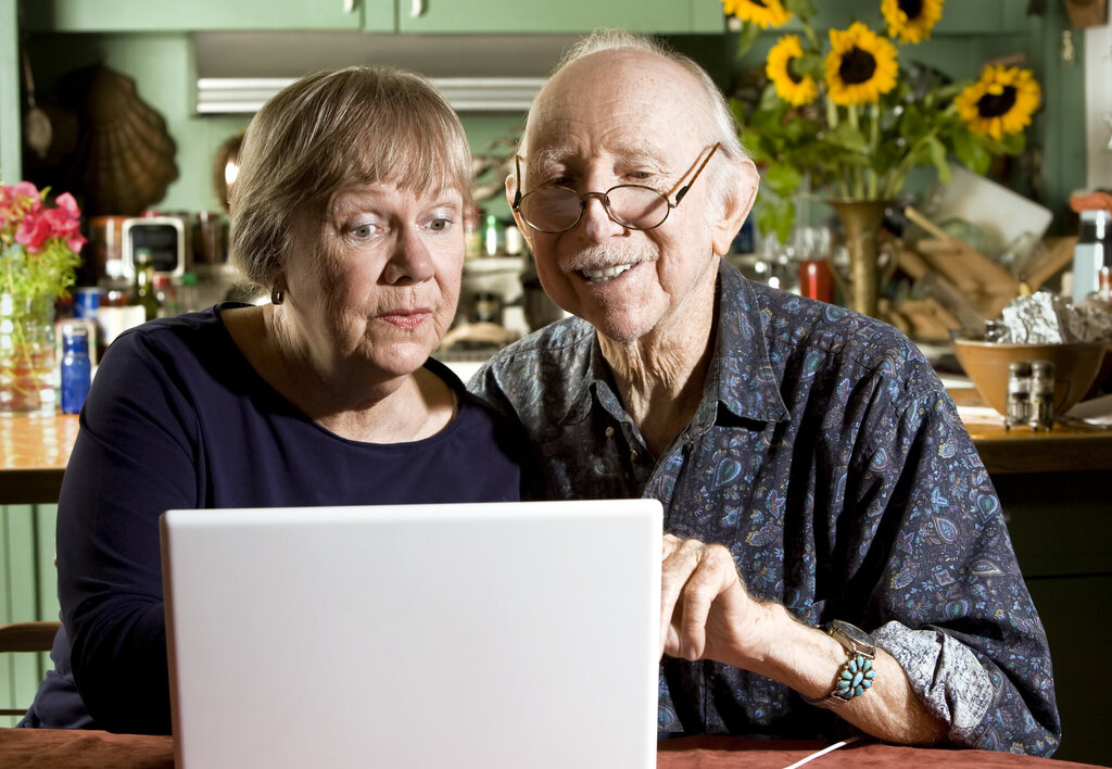 Bildet viser to eldre personer som sitter foran en laptop
