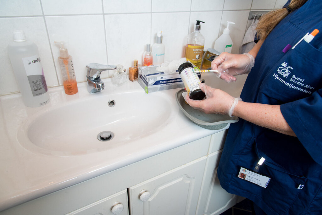 Bildet viser en hjemmesykepleier med en urinstrimmeltest på badet til brukeren