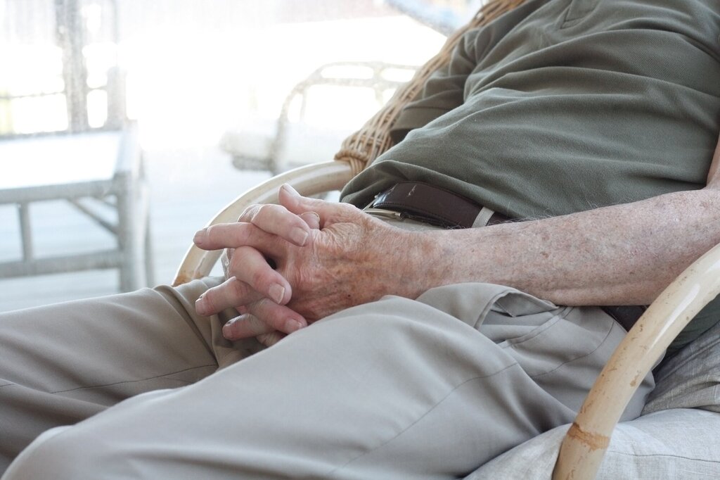 Bildet viser deler av en eldre person som sitter med hendene i fanget.
