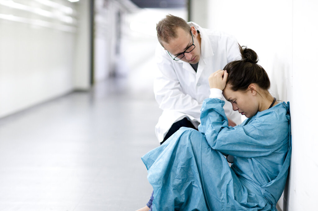 Bildet viser en kvinnelig sykehusansatt som får trøst av en mannlig i en korridor.