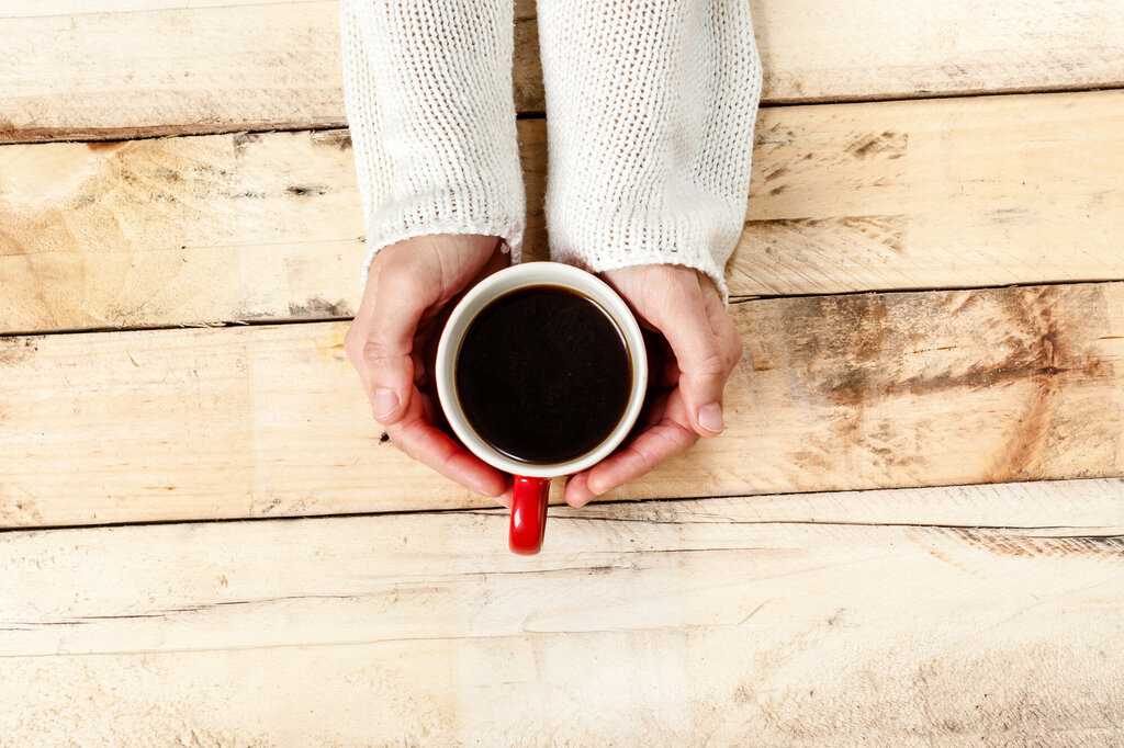 En kvinnes hender holder en kopp med kaffe på et rustikt trebord