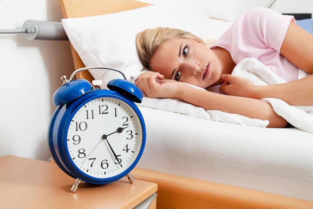 Bildet viser en kvinne som ligger i sengen og ser på vekkerklokken.