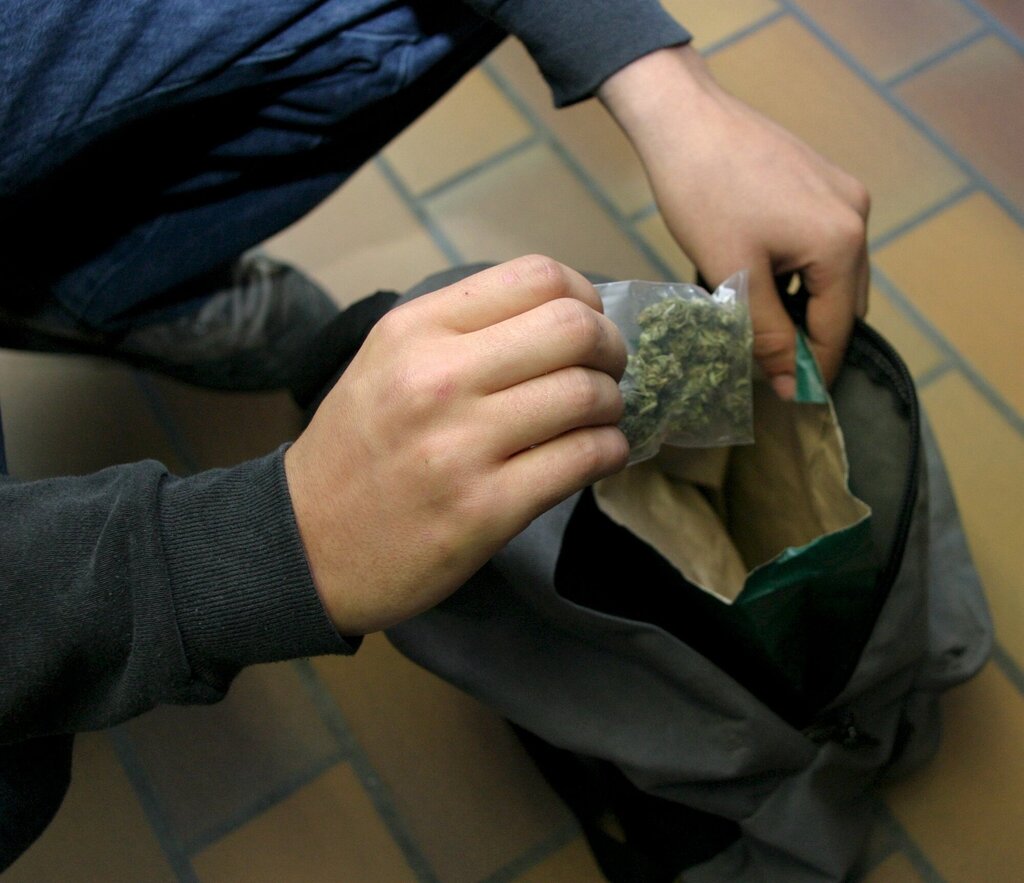 Bildet viser en ungdom som tar opp en pose marihuana av skolesekken