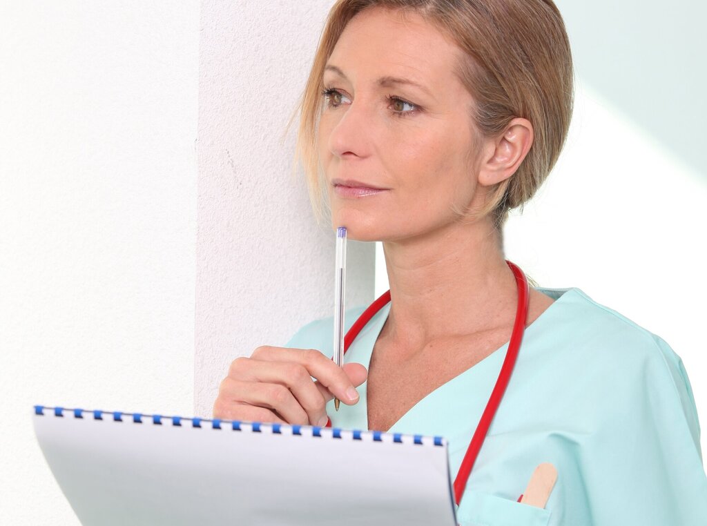 En kvinnelig sykepleier står og tenker med en penn og skriveblokk