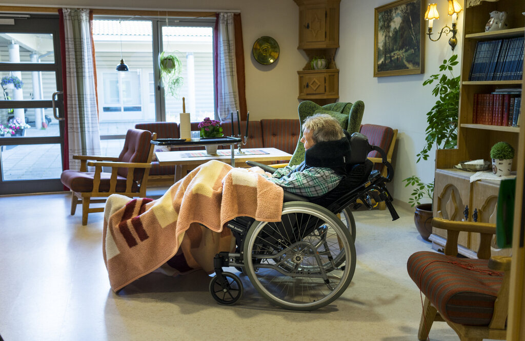 Bildet viser en eldre kvinne liggende i en rullestol i en stue på et behandlingssenter.  