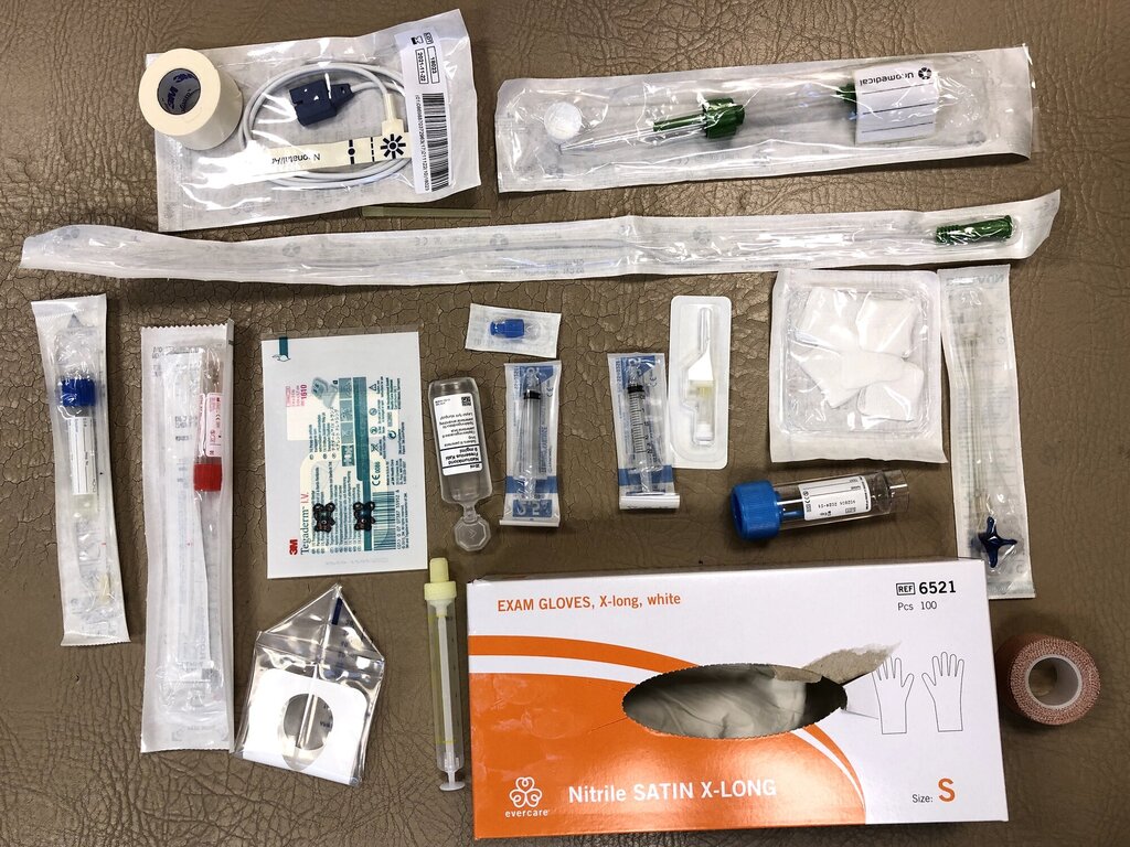 medisiner, hansker og ledninger innpakket i plast og papi, plassert på sykehusbenk 