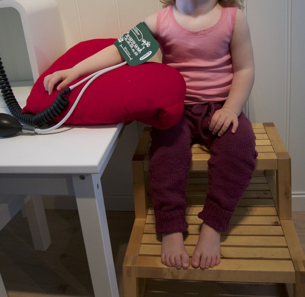 Bildet viser et barn som sitter på en krakk med støtte for beina og får blodtrykket sitt målt