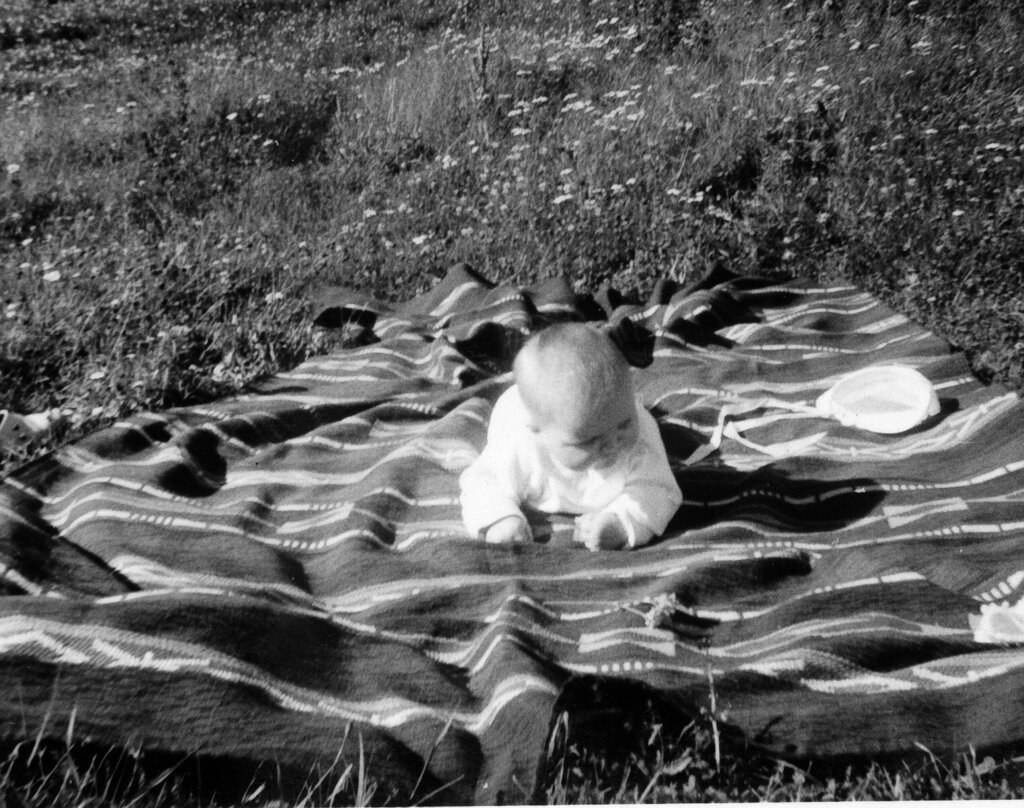 Bildet viser Karin Jonli som baby liggende på et teppe på gresset.