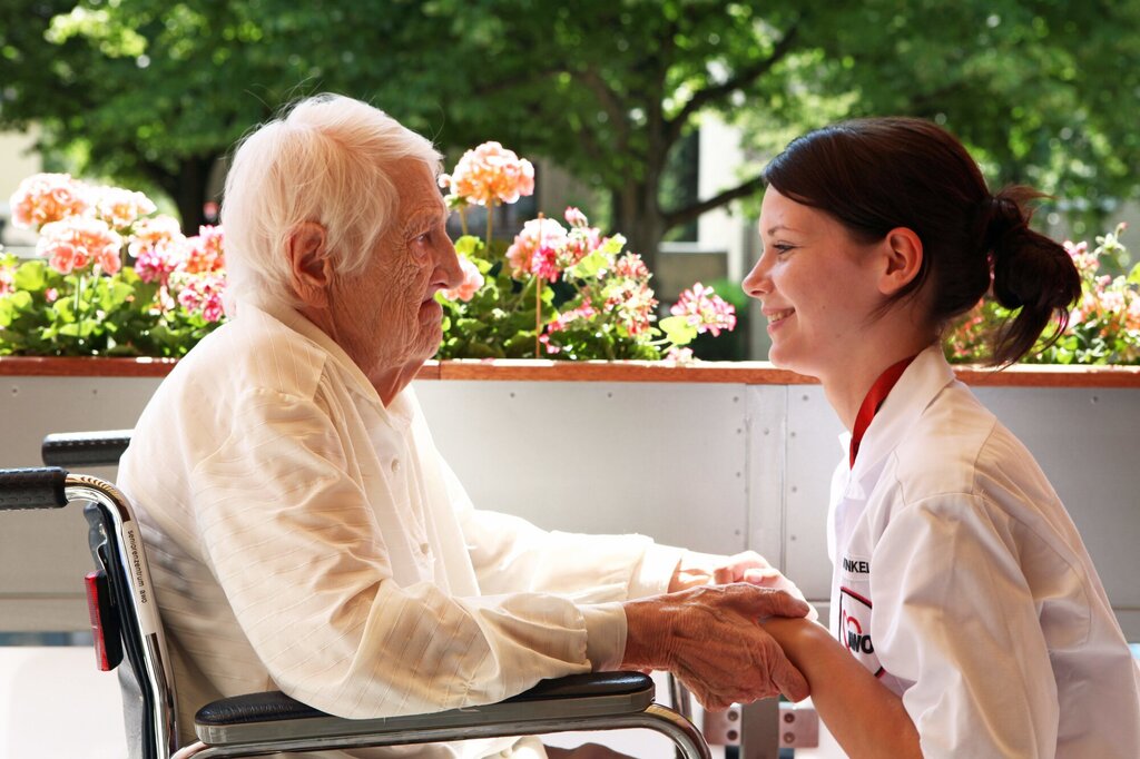 Bildet viser en sykepleier som holder en eldre person i hendene