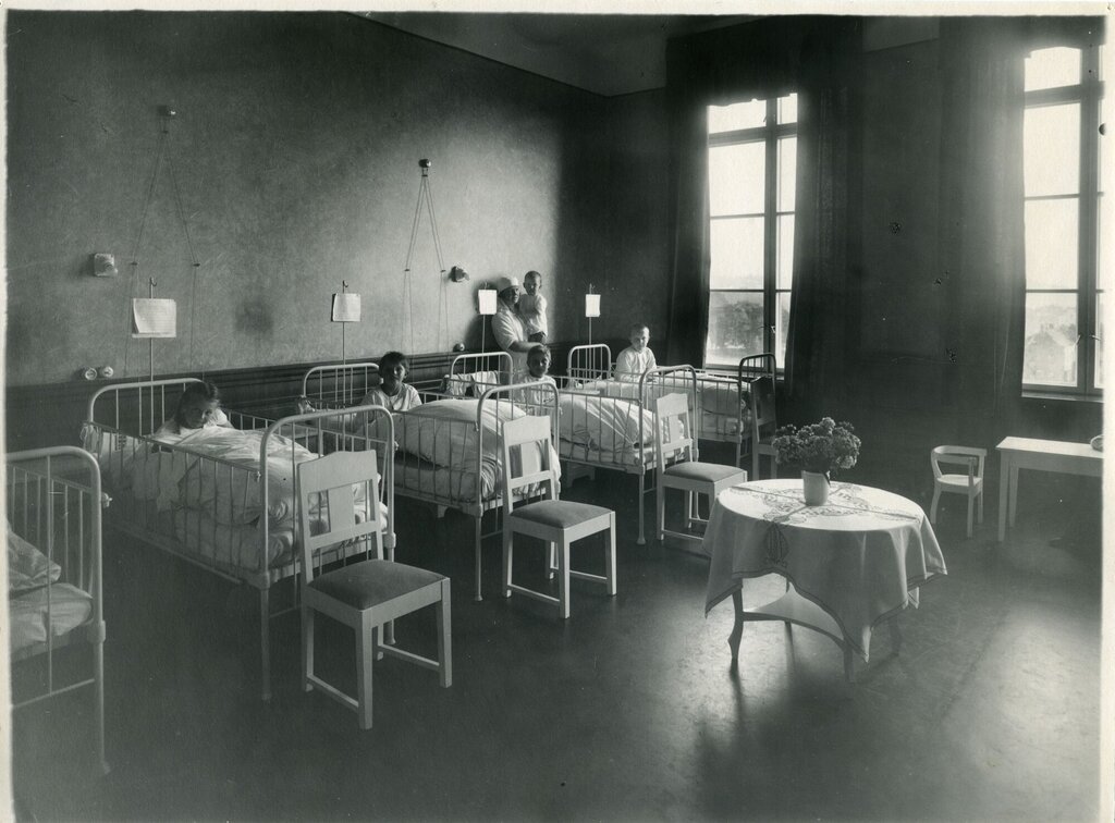 Bildet viser en sykehussal med flere senger og barn.