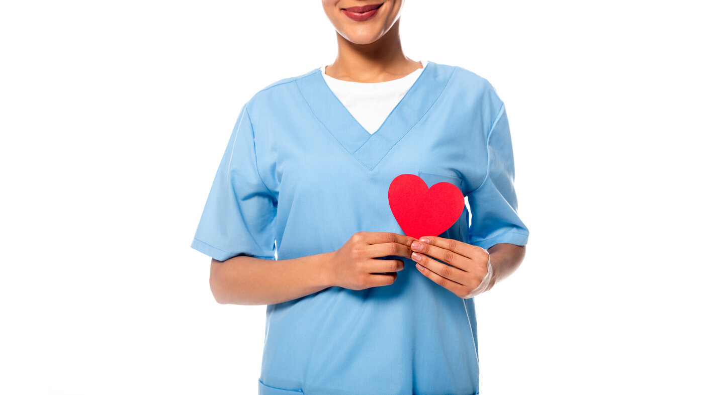 Bildet viser en sykepleier som holder et papirhjerte foran hjertet sitt