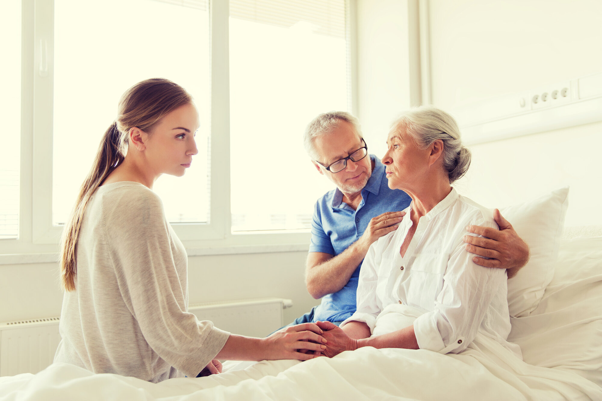 Syk eldre kvinne med familien Bildet viser en eldre, syk dame i senga. Familien sitter på sengekanten, og en mann holder rundt henne.