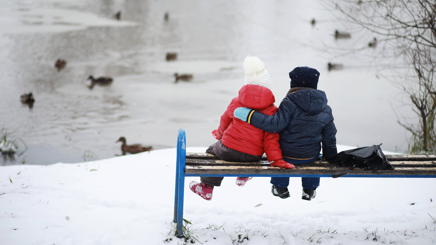 Bildet viser to barn som sitter på en benk og ser på et vann med ender på