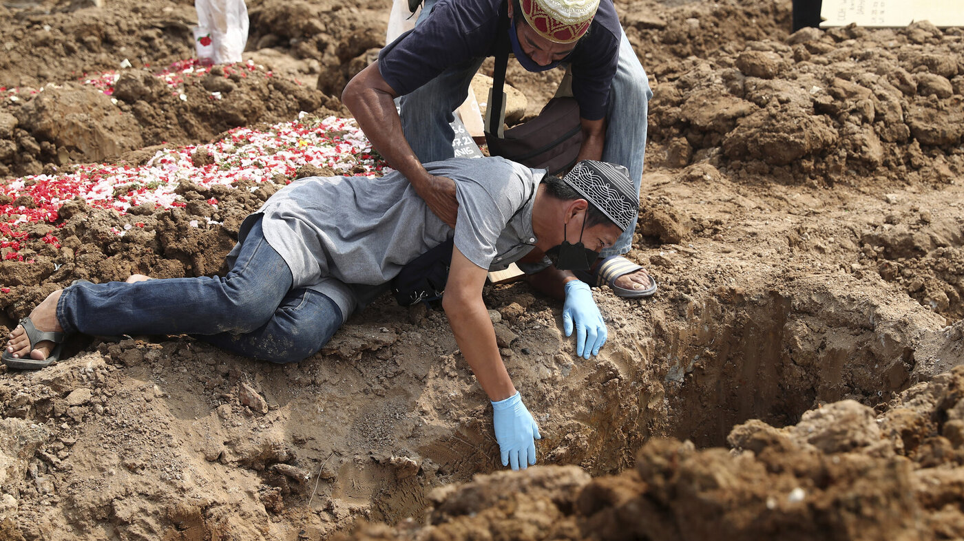 Bildet viser en mann som sørger ved siden av en grav over et familiemedlem som har dødd av covid-19