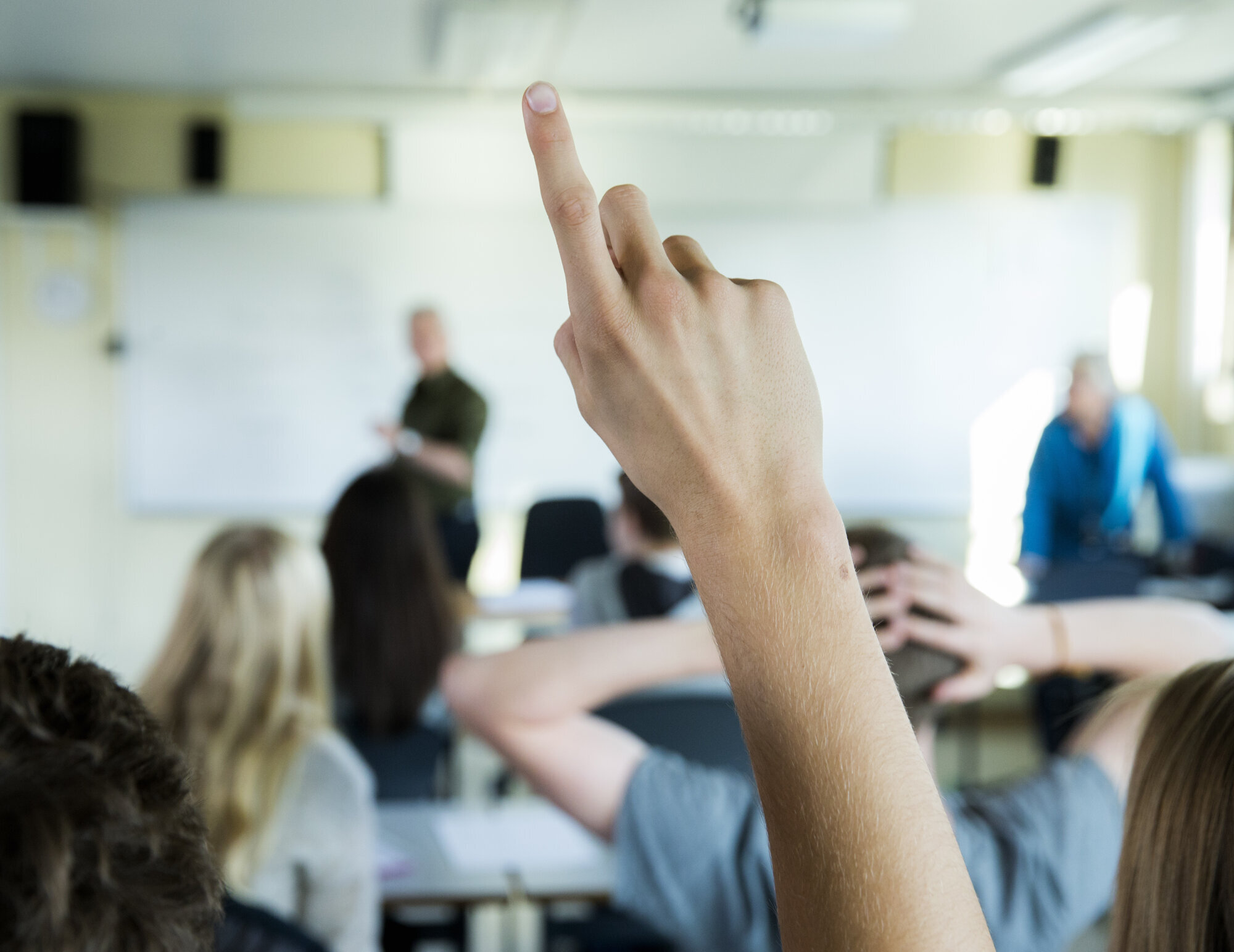 Skole, klasserom Bildet viser en hånd som rekkes opp i et klasserom.
