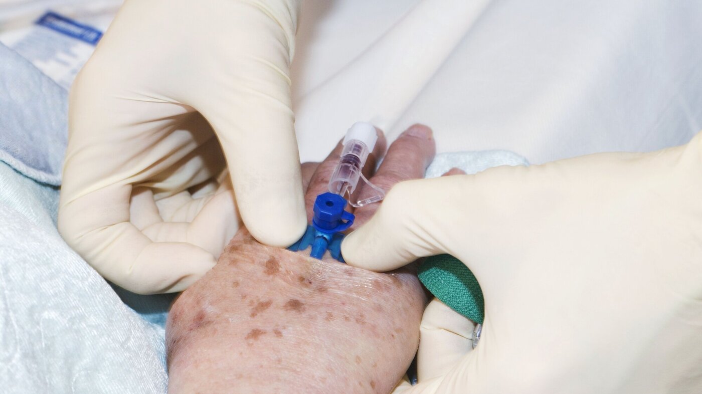 Innleggelse av perifert venekateter Bildet viser hendene til en sykepleier, som holder på å legge inn perifert venekateter på en hånd til en eldre person