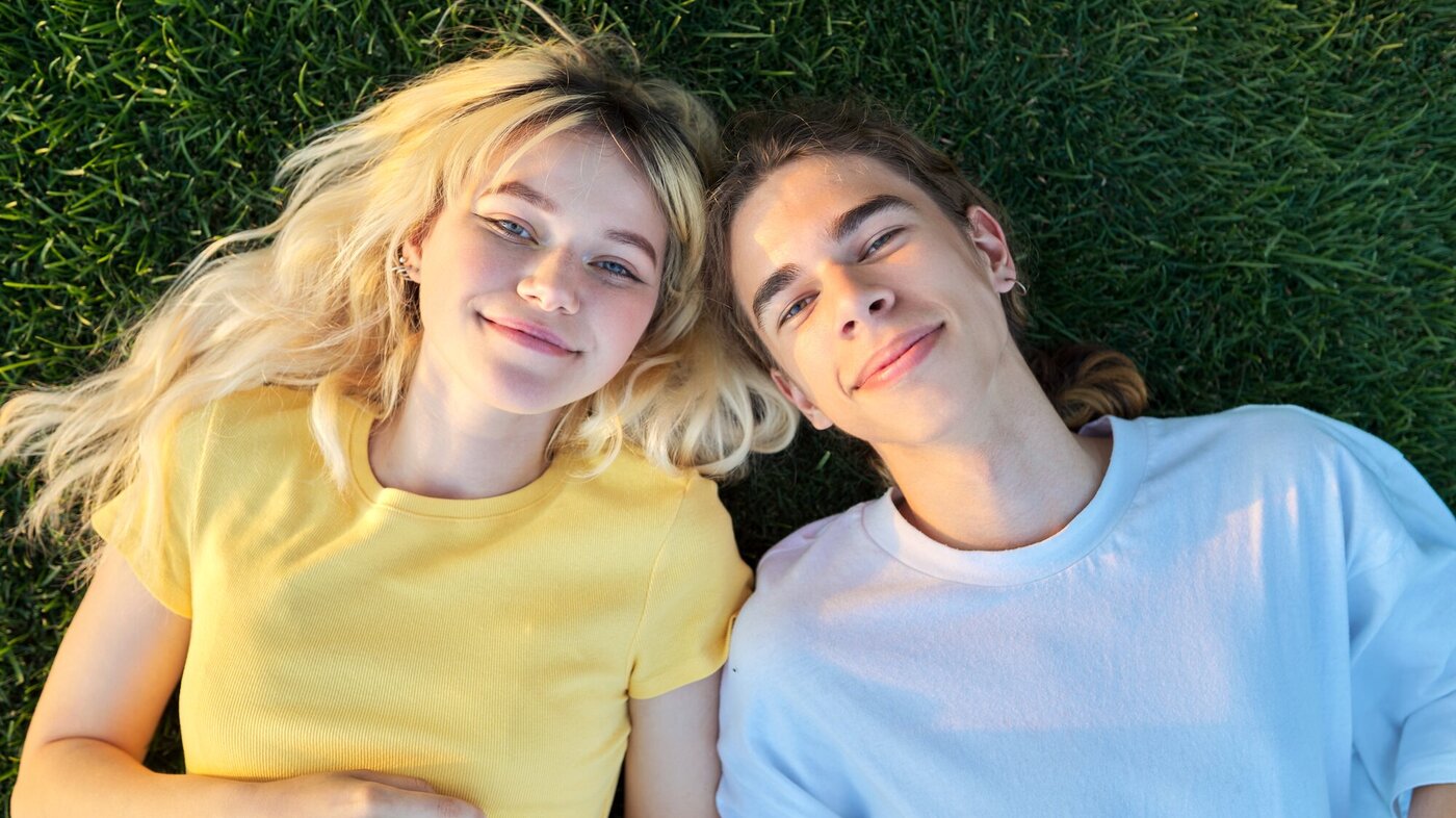 Bildet viser to smilende ungdommer som ligger på gresset
