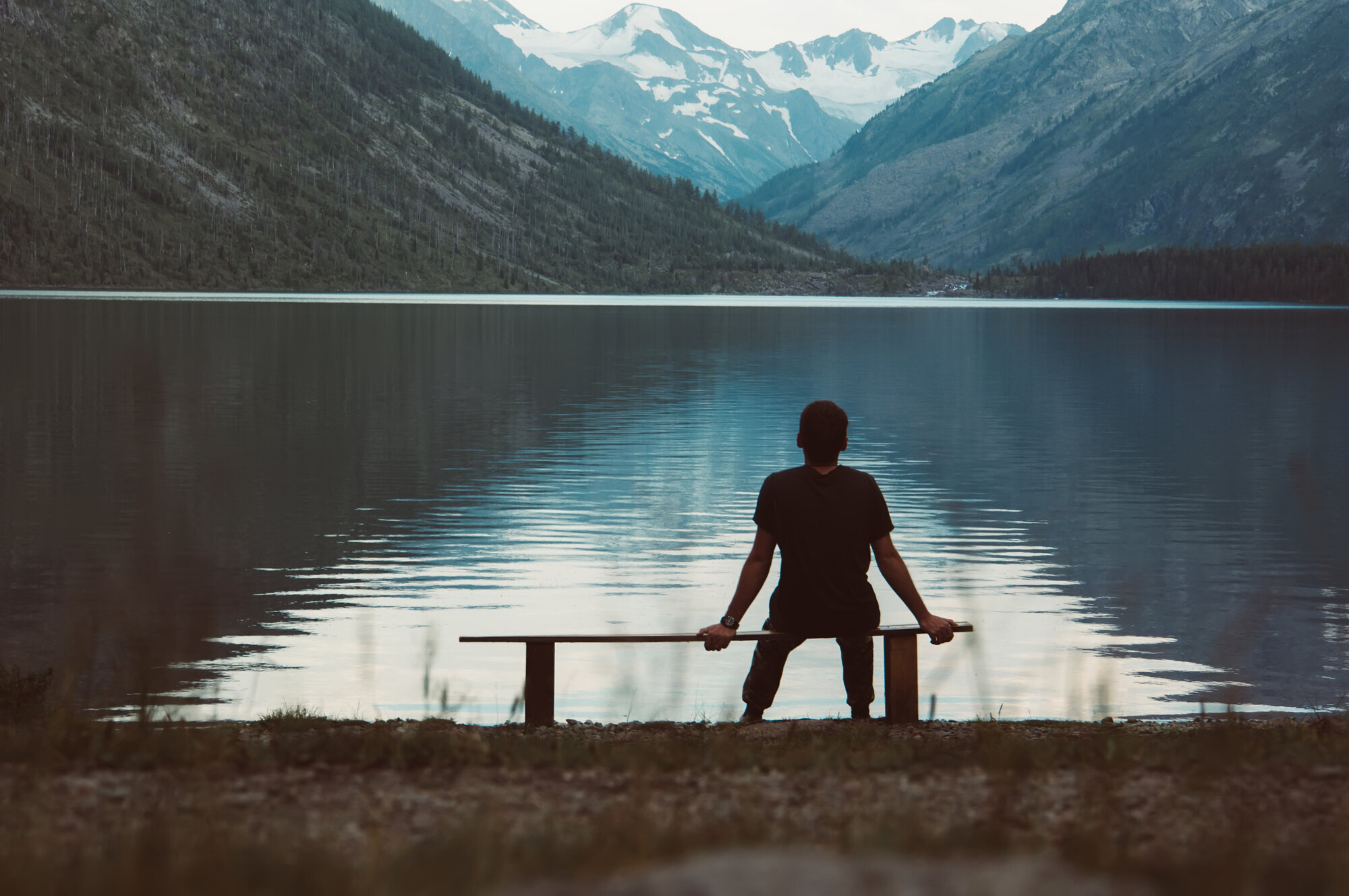Mann i natur Bildet viser en mann som sitter alene på en benk og ser utover fjorden
