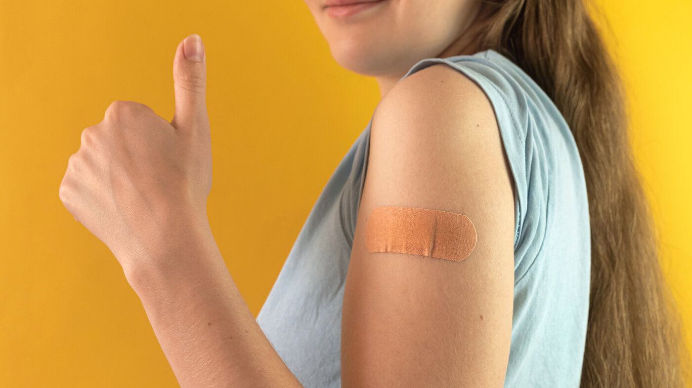 Bildet viser en ung kvinne med tommelen opp etter å ha tatt vaksine. 