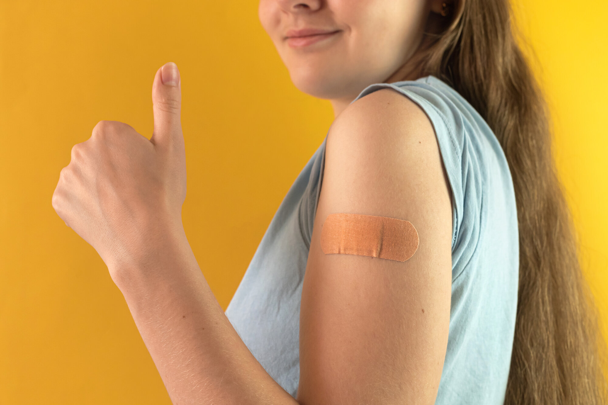Vaksine Bildet viser en ung kvinne med tommelen opp etter å ha tatt vaksine.