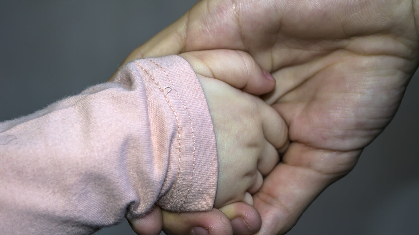 Bildet viser hånden til et lite barn i en voksen hånd