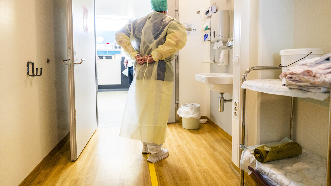 Bildet viser et helsepersonell utenfor en sluse som ikler seg smittevernutstyr.