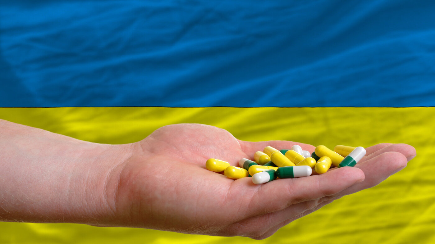 Bildet viser en hånd som holder piller, i bakgrunnen ses litt av det ukrainske flagget.