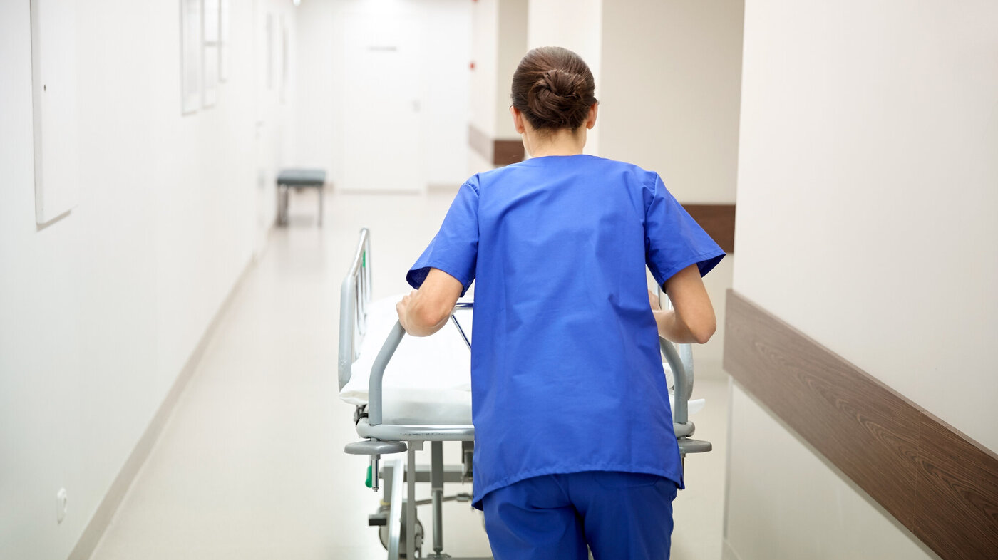 Travel sykepleier med seng i sykehuskorridor