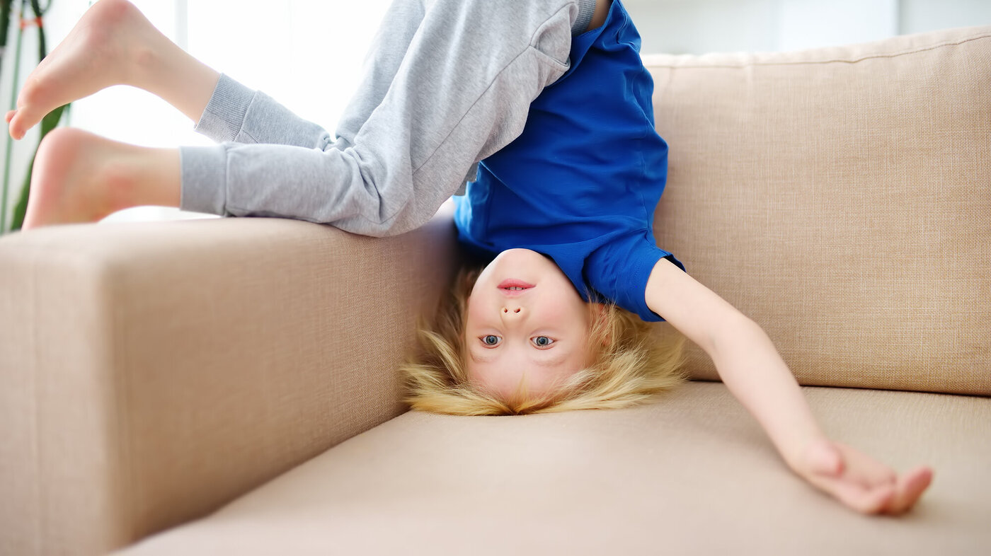 Et barn står på hodet i sofaen