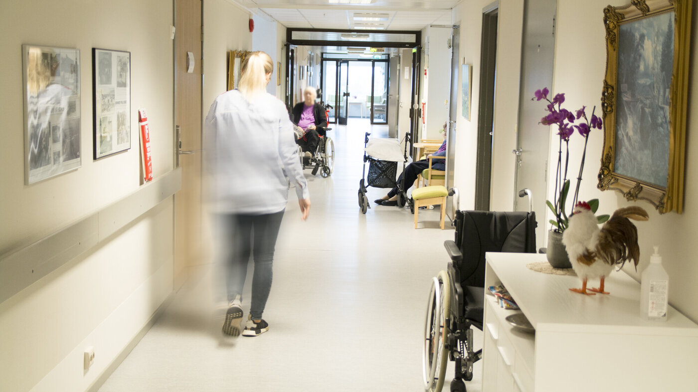 Sykehjem Sykepleier som går nedover en sykehjemskorridor.