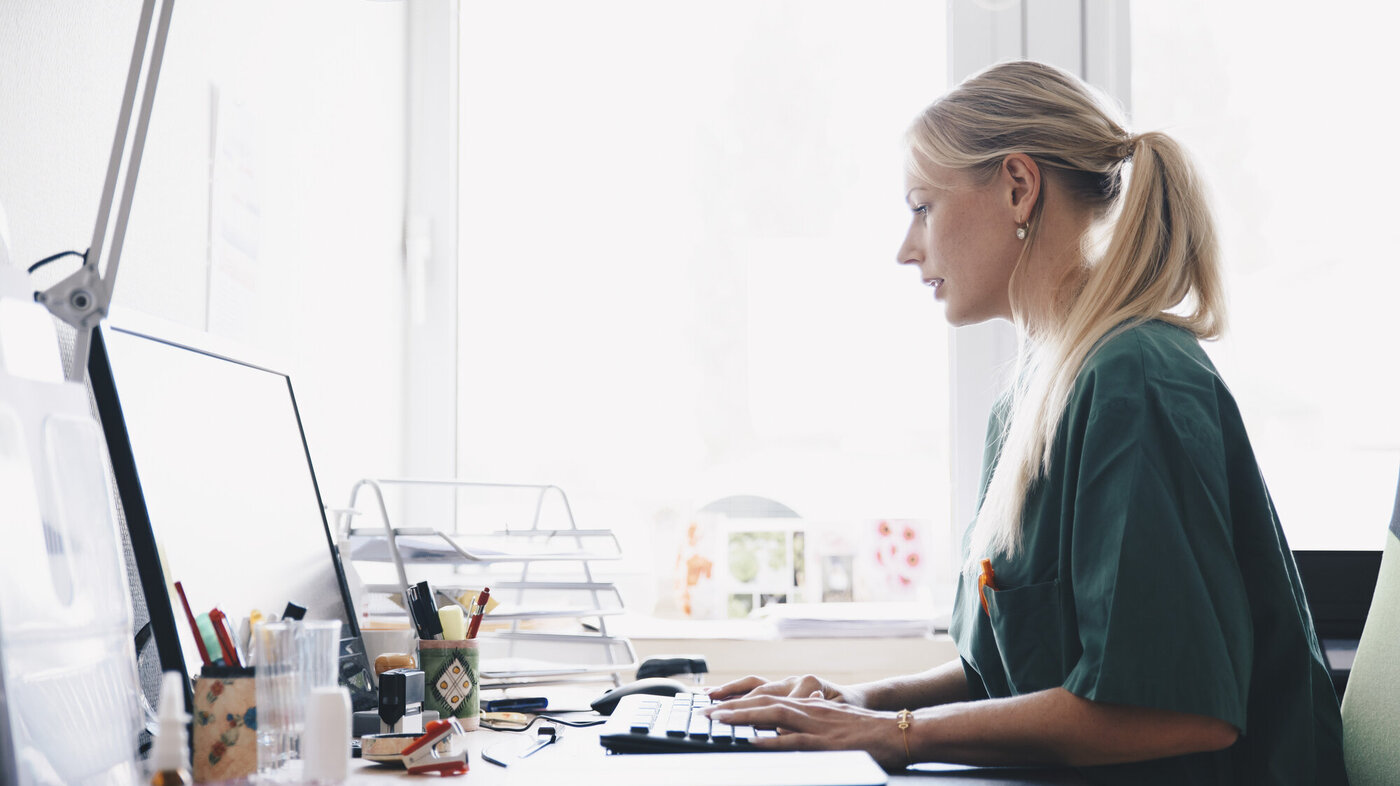 Sykepleier Bildet viser en ung kvinnelige sykepleier som jobber foran en datamaskin